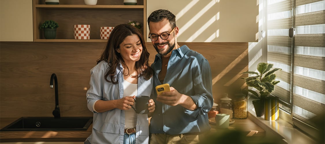 Couple smiling at good news on their phone in kitchen with unique lighting