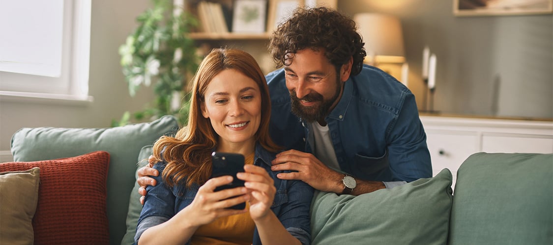 iStock-2219950113 - Couple Smiling at Phone on Couch